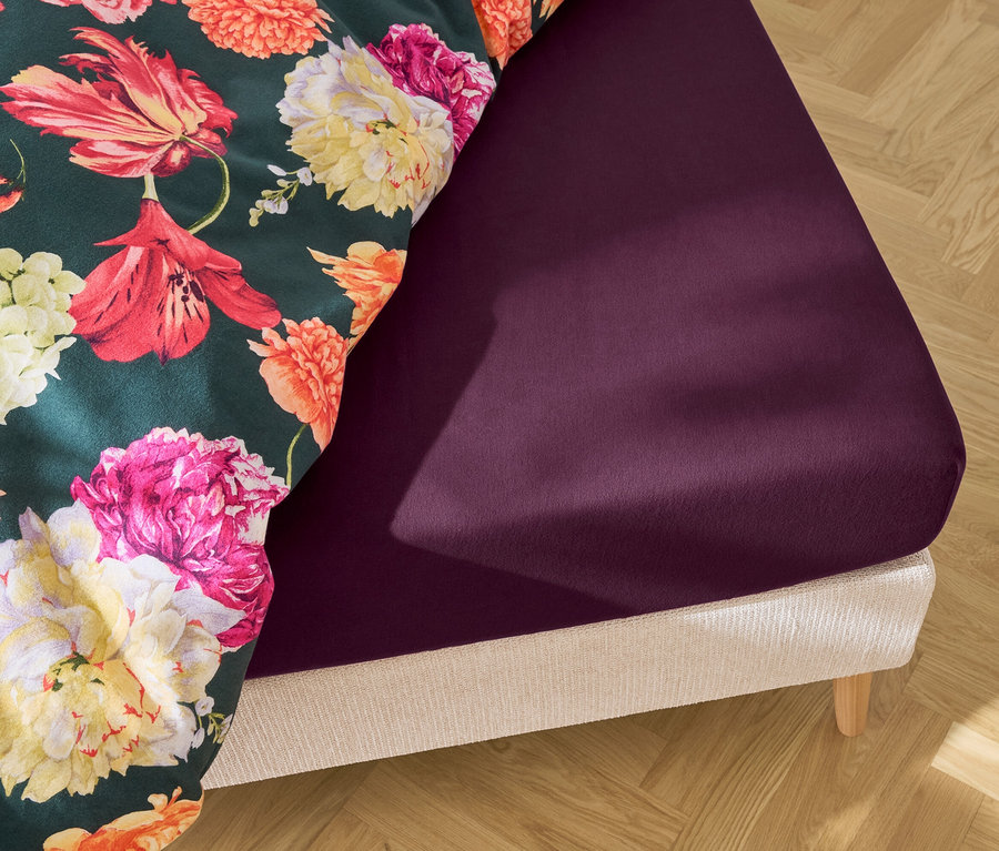 Gros plan d'un lit avec un drap-housse violet foncé et une couette à motifs floraux.