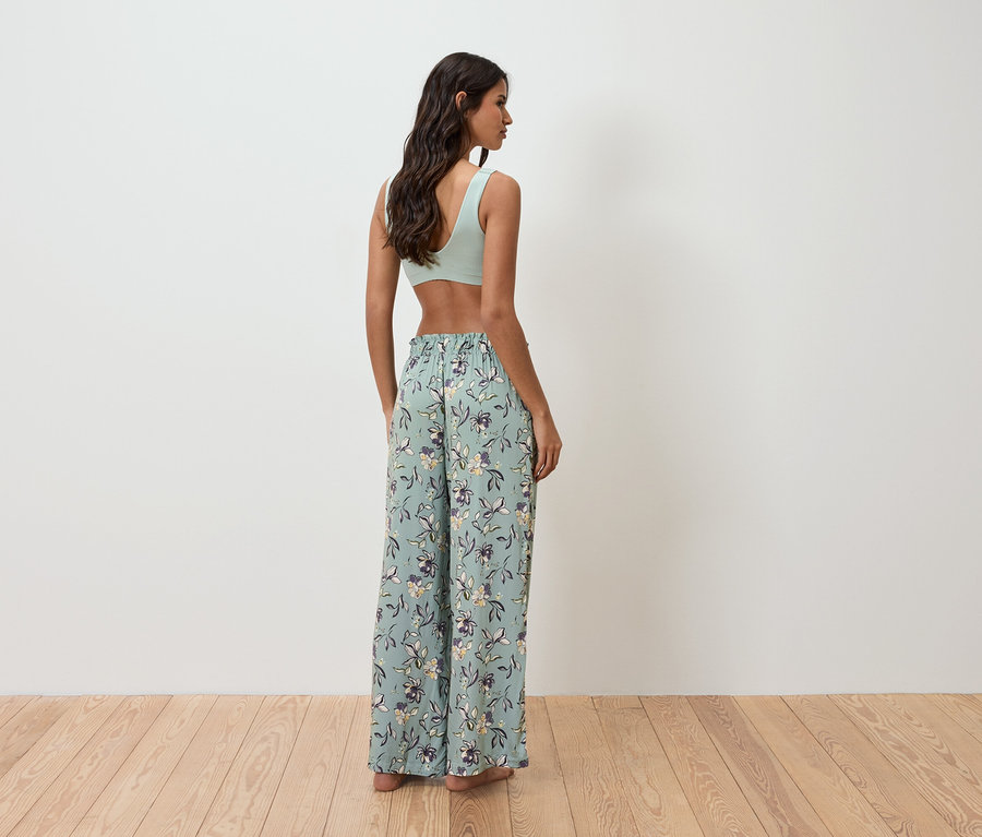 Une femme, vue de dos, porte un haut vert clair et un pantalon ample à motifs floraux.