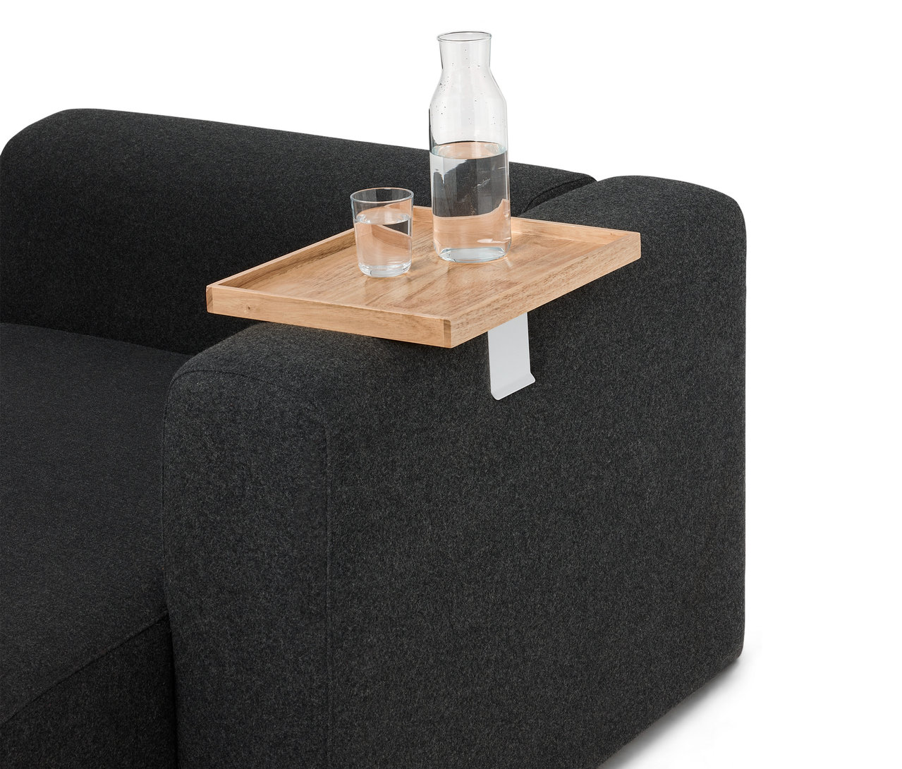 Sur un canapé gris se trouve un plateau en bois avec une bouteille et un verre d'eau.