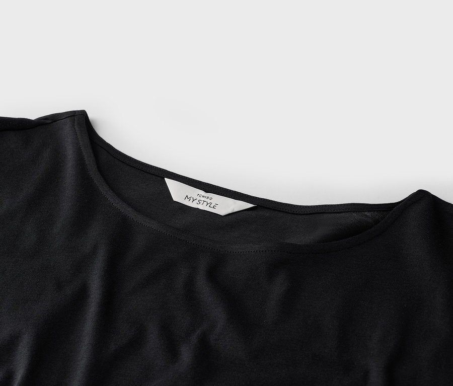 Gros plan d'un t-shirt noir avec une étiquette blanche 'TCHIBO MY STYLE' sur le col.