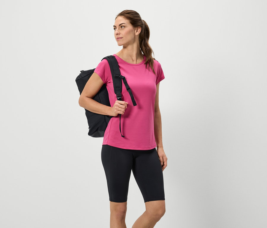 Femme avec sac à dos noir, t-shirt rose et short noir.