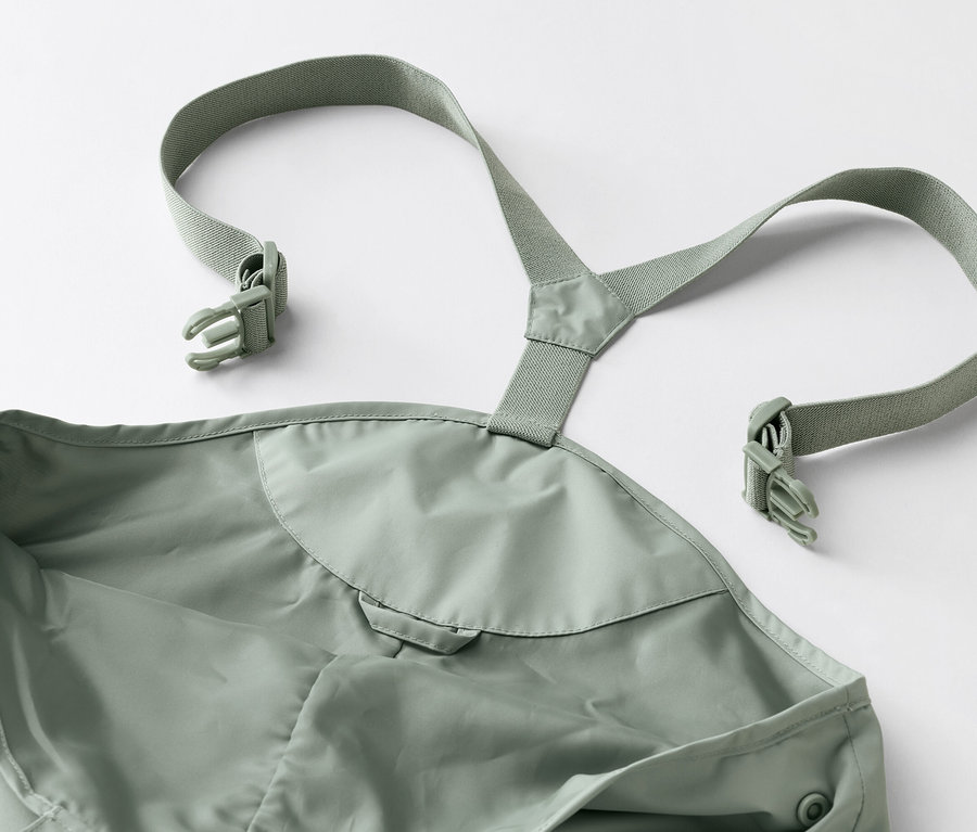 Gros plan d'une salopette de pluie verte avec des bretelles et des boucles sur un fond blanc.
