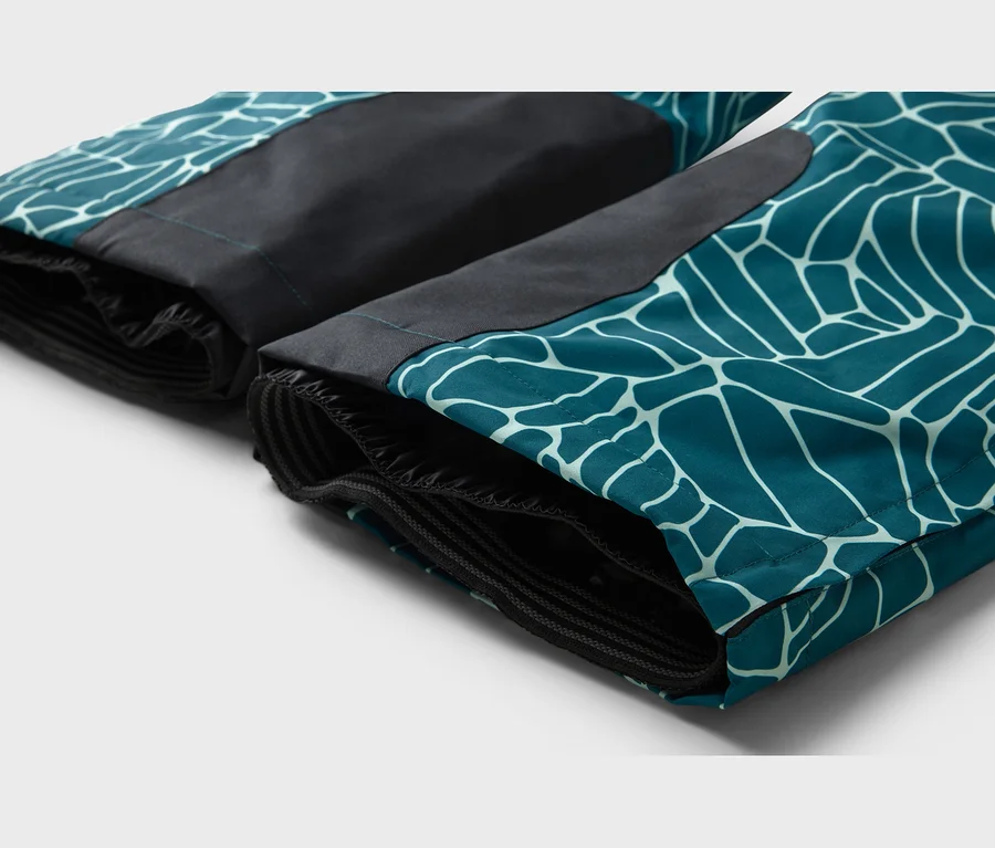 Deux jambes de pantalon turquoise avec un motif géométrique blanc et des empiècements noirs, avec des poignets élastiques à l'ourlet.