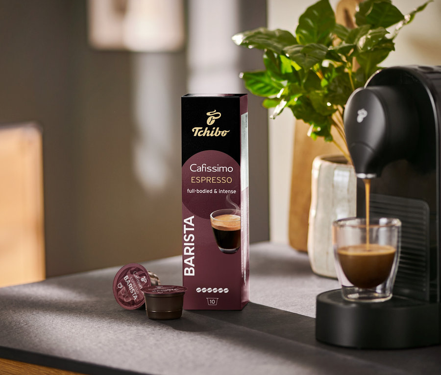 Un espresso coule dans un verre depuis une machine Cafissimo BARISTA, à côté d'un paquet de 10 capsules.