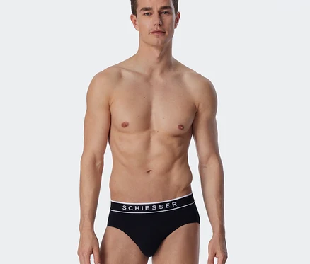 Homme torse nu portant un slip Rio SCHIESSER noir avec une ceinture à logo blanc.