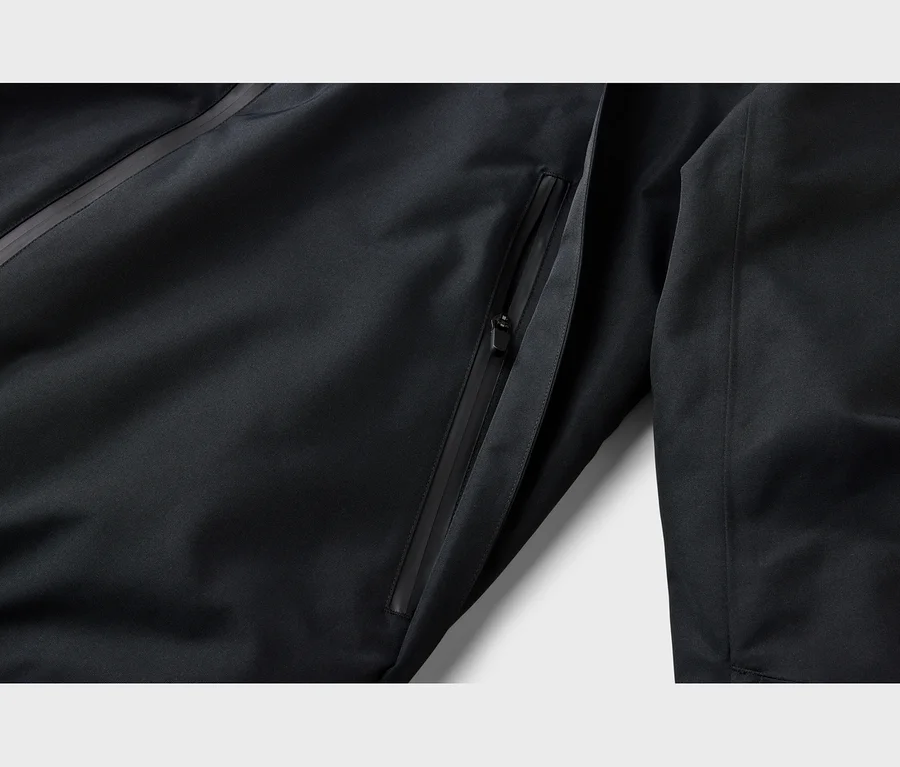 Gros plan d'une veste noire avec une poche zippée partiellement ouverte et une tirette de fermeture éclair noire. Une couture diagonale traverse le coin supérieur gauche.