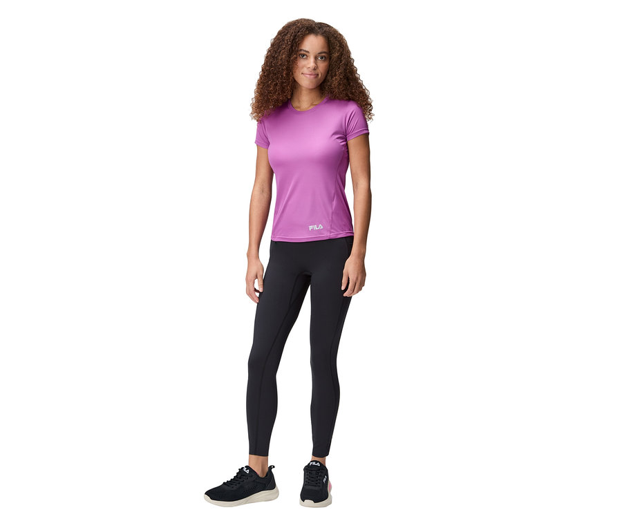Une femme aux cheveux bouclés porte un T-shirt technique pour femme FILA violet, un legging noir et des baskets noires.