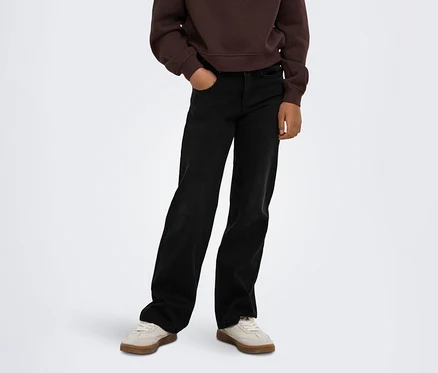 Personne portant un sweat-shirt marron, un jean noir large avec une main dans la poche et des baskets beige clair.