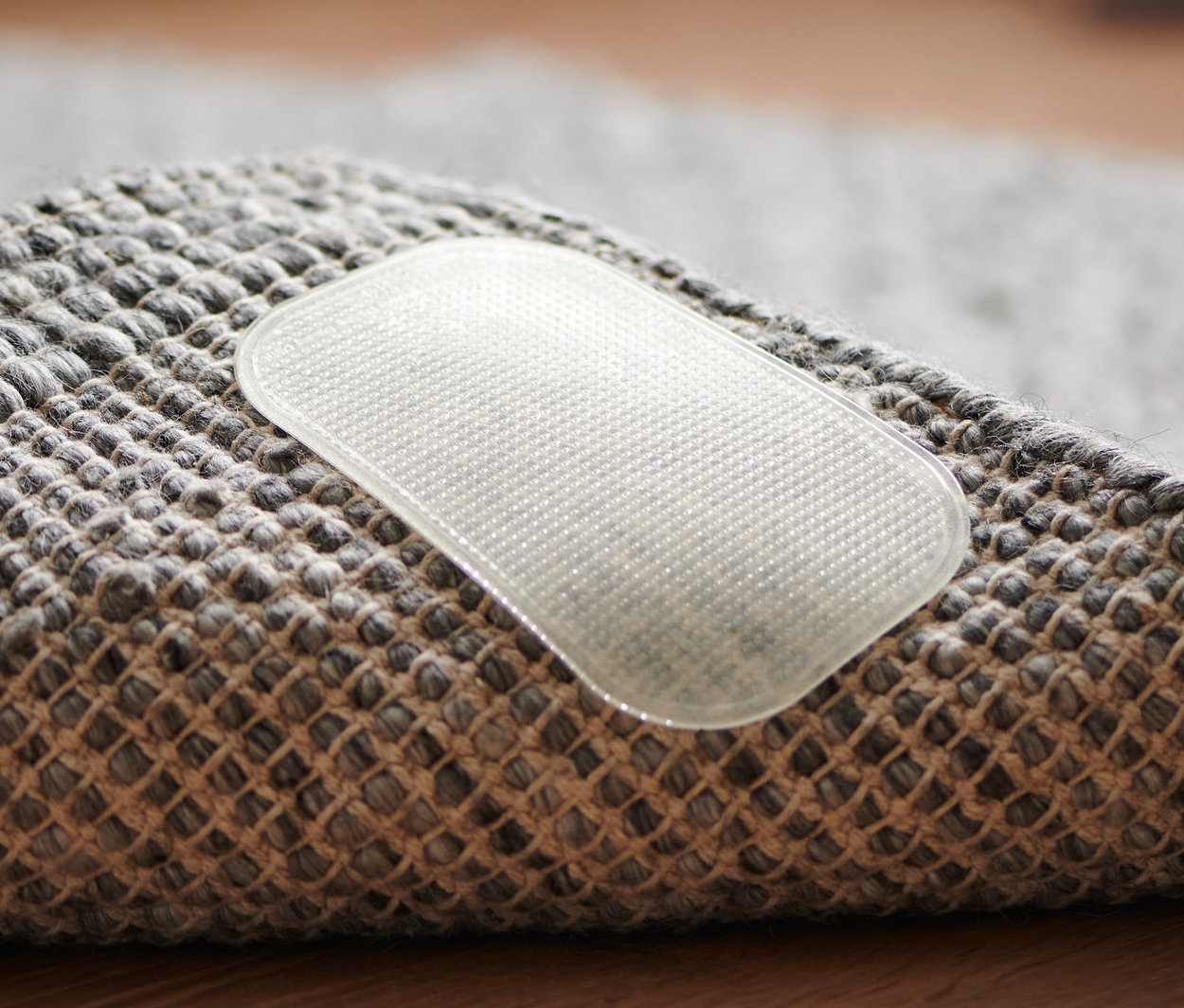 Gros plan sur le coin d'un tapis gris avec un 4 patins antidérapants de tapis transparent.