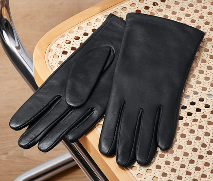 Des gants en cuir noirs sont posés sur une chaise en rotin.