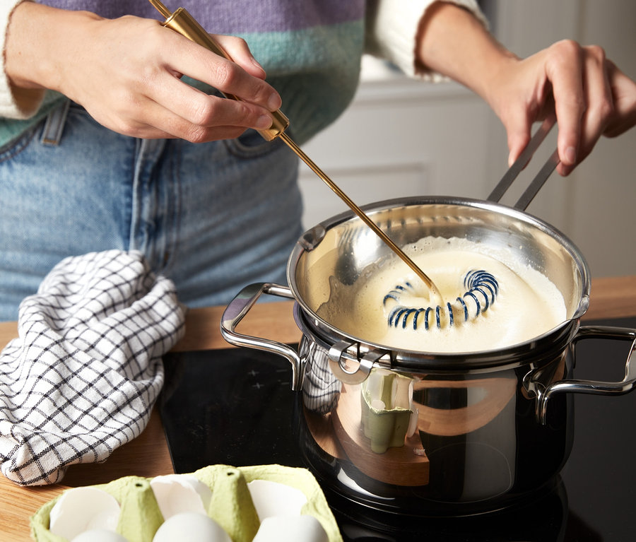 Une personne mélange des œufs dans une casserole avec un fouet professionnel.
