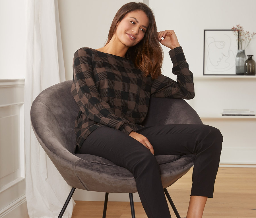 Une femme est assise dans un fauteuil et porte un sweat-shirt à carreaux.