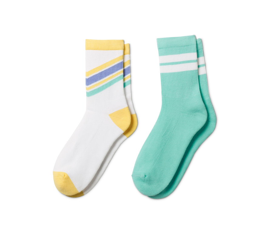 Deux paires de chaussettes de tennis en coton bio. Une paire est blanche avec des détails jaunes et des rayures colorées, l'autre paire est turquoise avec des rayures blanches.