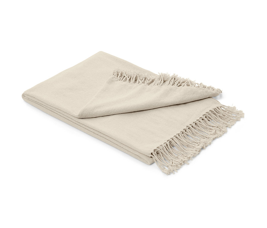 Une couverture chenille beige à franges, pliée sur un fond blanc.