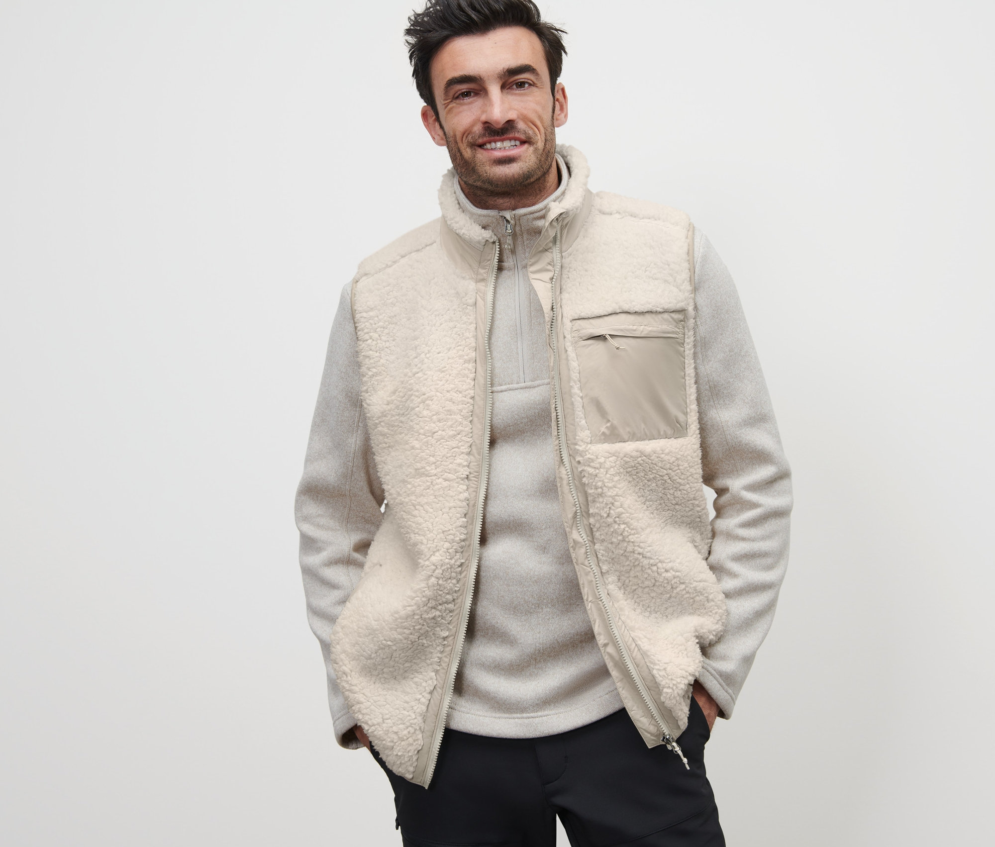 Un homme porte un gilet en peluche par-dessus un pull clair à fermeture éclair.