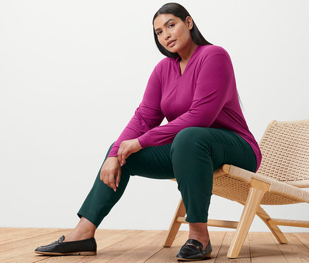 Femme assise sur une chaise, portant un t-shirt manches longues framboise avec encolure en V et un pantalon stretch.
