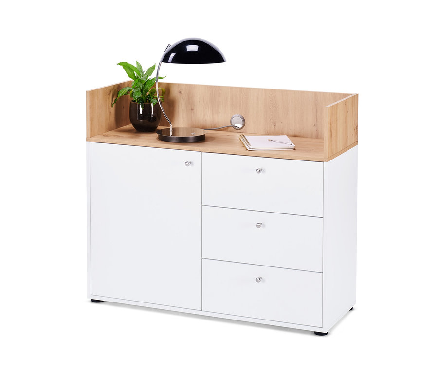 Un buffet avec tiroirs et porte avec une plante en pot, une lampe et un carnet dessus.