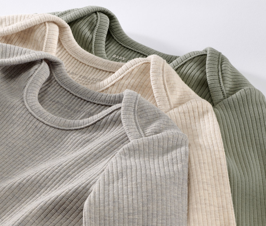 Gros plan sur trois t-shirts côtelés pour bébé en gris, crème et vert olive.
