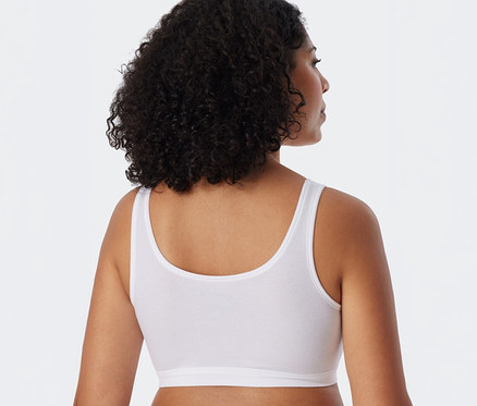 Femme de dos, la tête légèrement tournée vers la droite, portant une brassière SCHIESSER blanche.