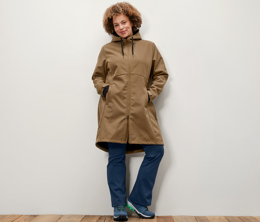 Une femme pose portant un manteau en softshell couleur nougat et un pantalon jazz thermique.