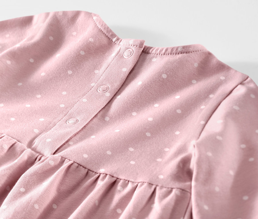 Gros plan sur une robe en jersey rose pour bébé avec des pois blancs et une fermeture boutonnée.
