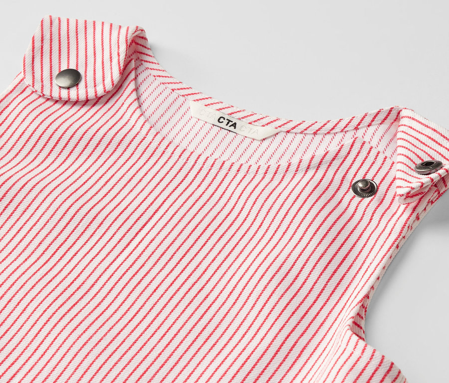Gros plan d'une robe-salopette tissée pour enfant avec des rayures rouges et des boutons métalliques.