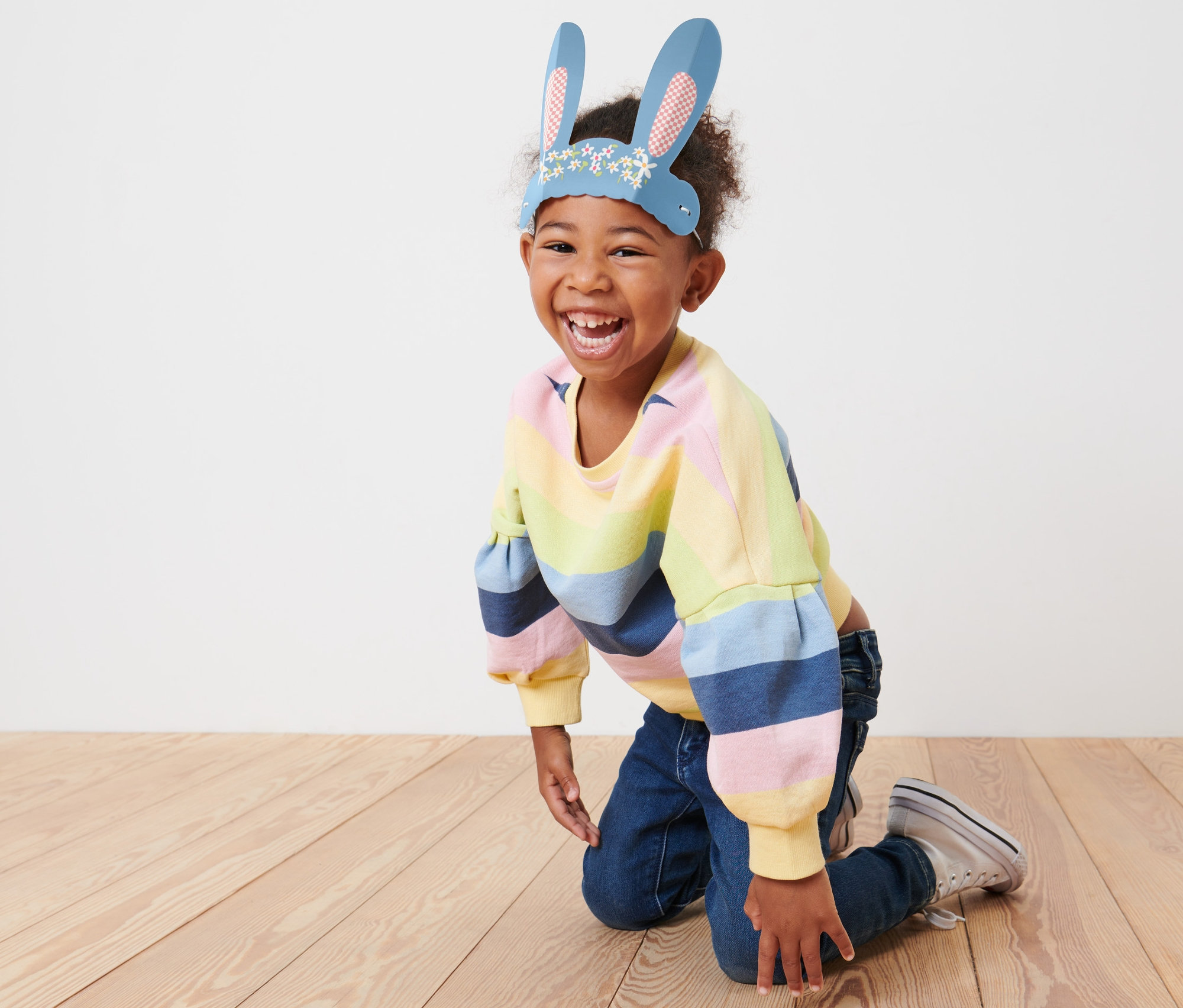 Un enfant souriant est agenouillé sur le sol et porte des oreilles de lapin en papier.