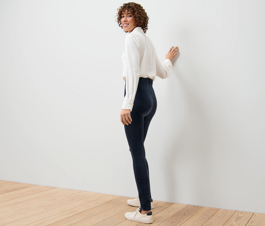 Femme regardant par-dessus son épaule posant en leggings en velours côtelé, une chemise blanche et des baskets.