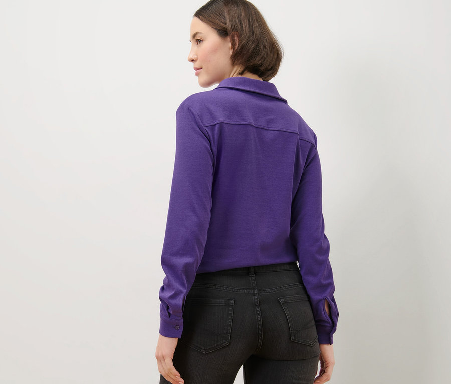 Une femme porte une blouse violette avec une patte de boutonnage et un jean noir.