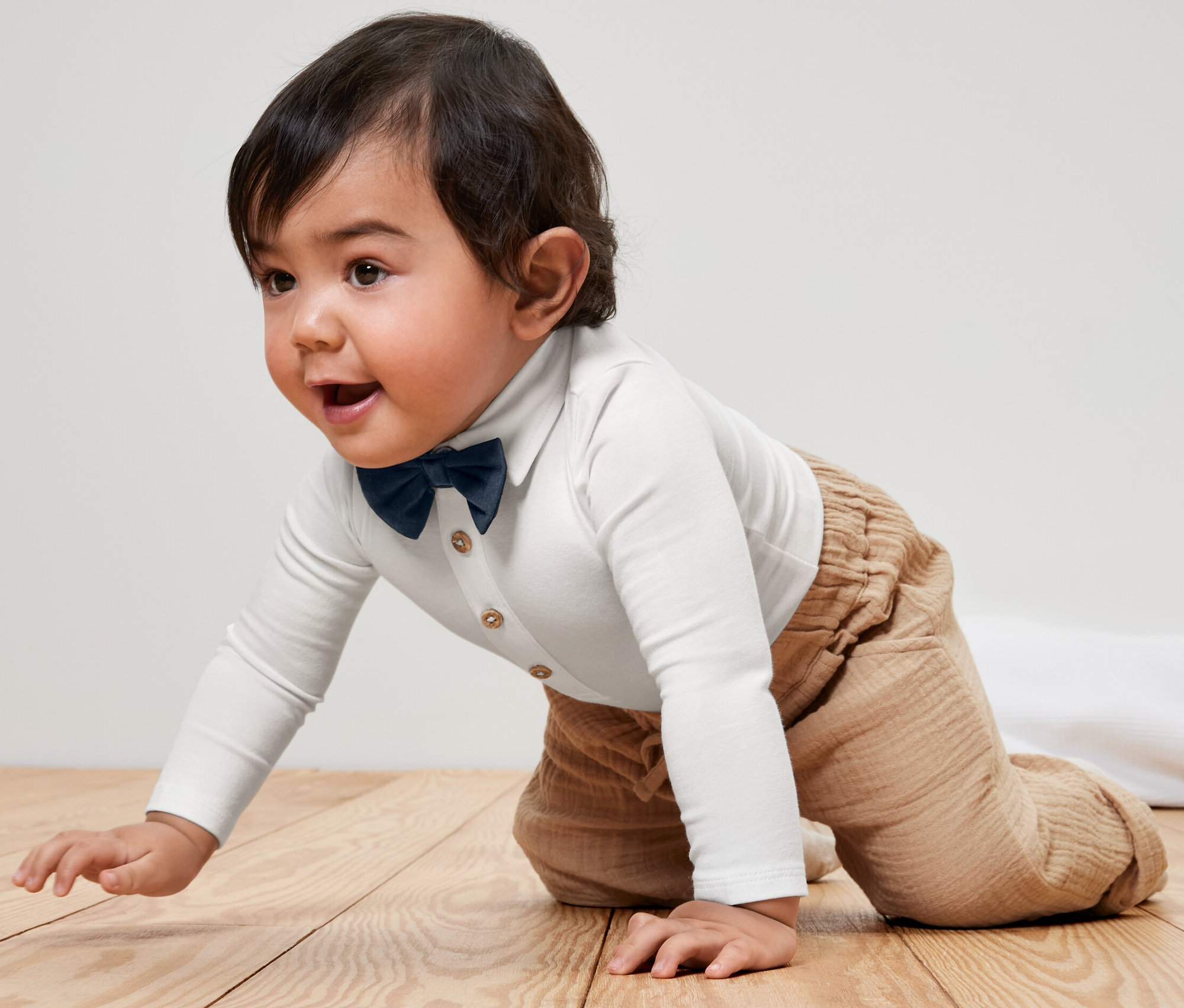 Bébé rampant en body avec nœud papillon sur un plancher en bois.