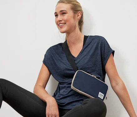 Une femme est assise par terre avec un sac multifonction en bandoulière.