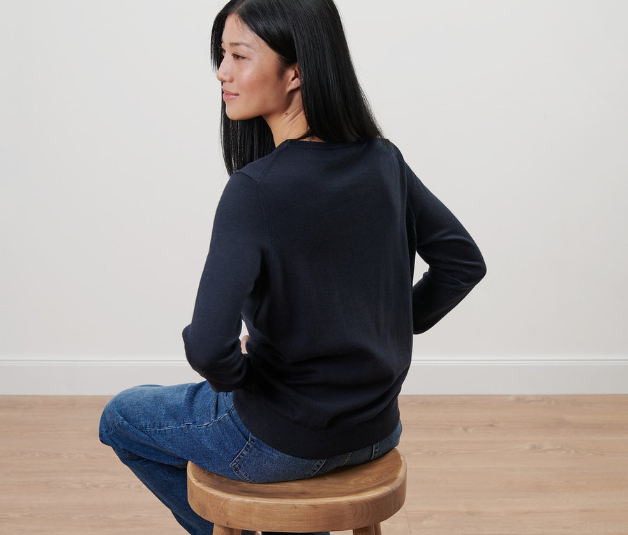 Une femme est assise sur un tabouret en bois et porte un pull en maille fine de mérinos bleu foncé.