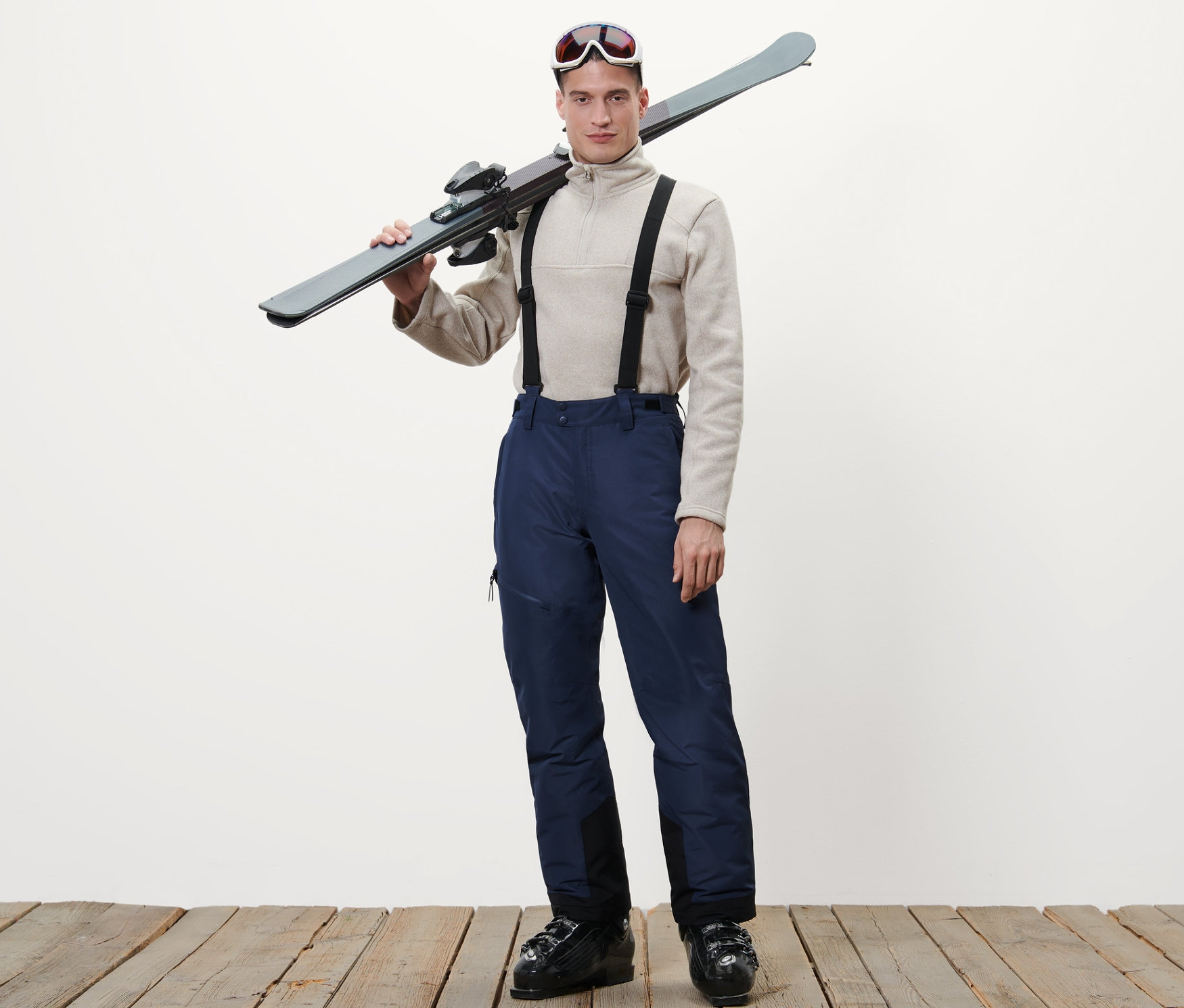 Un homme portant un pantalon de ski bleu porte des skis sur son épaule.