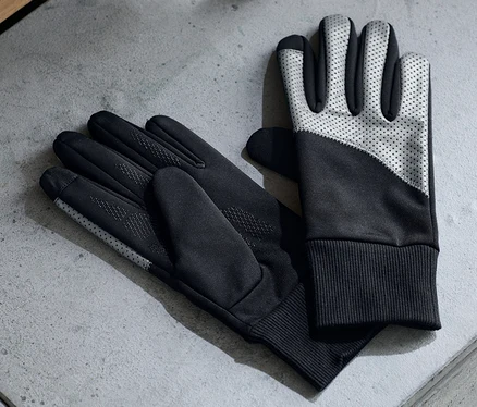 Deux paires de gants coupe-vent posées sur une surface grise à côté d'écouteurs et d'une bouteille d'eau.