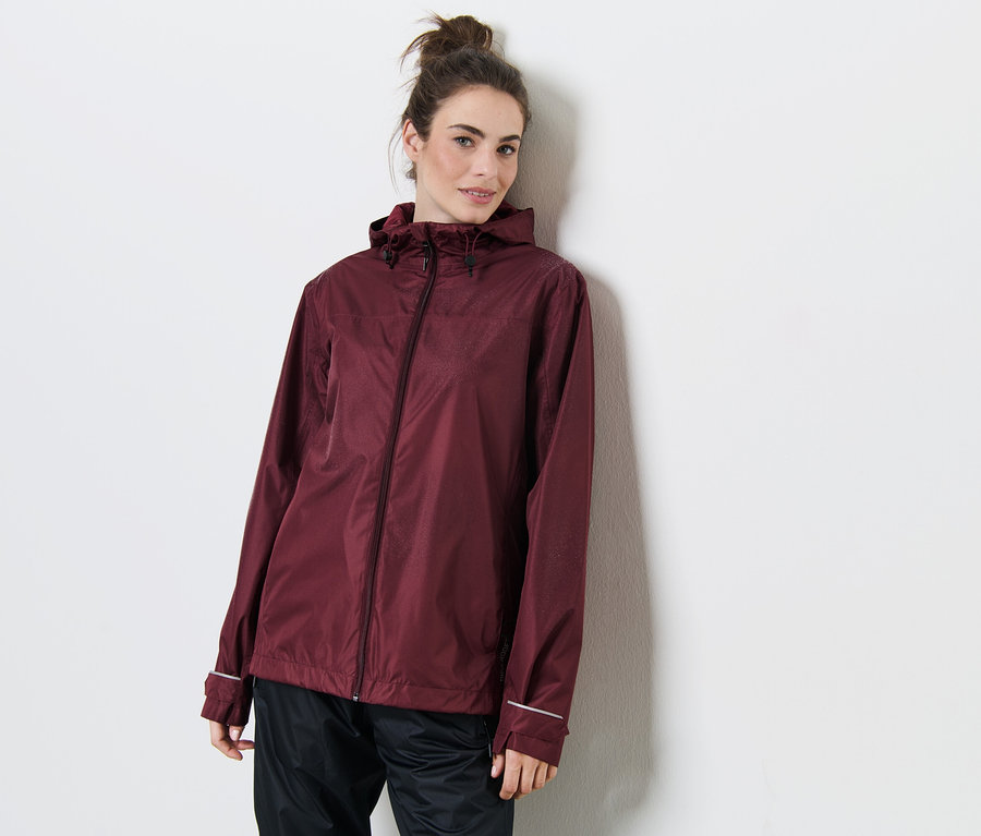 Une femme appuyée contre un mur porte une veste de pluie bordeaux.
