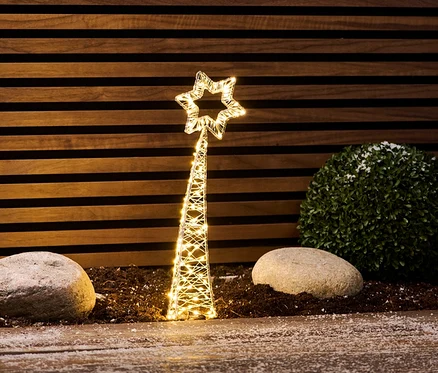 Une petite étoile filante LED se dresse entre des pierres et un buisson.