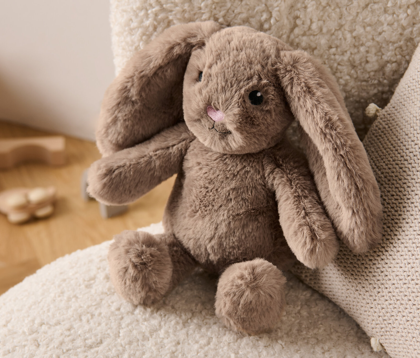 Un lapin en peluche est posé sur un fauteuil crème à côté d'un coussin.