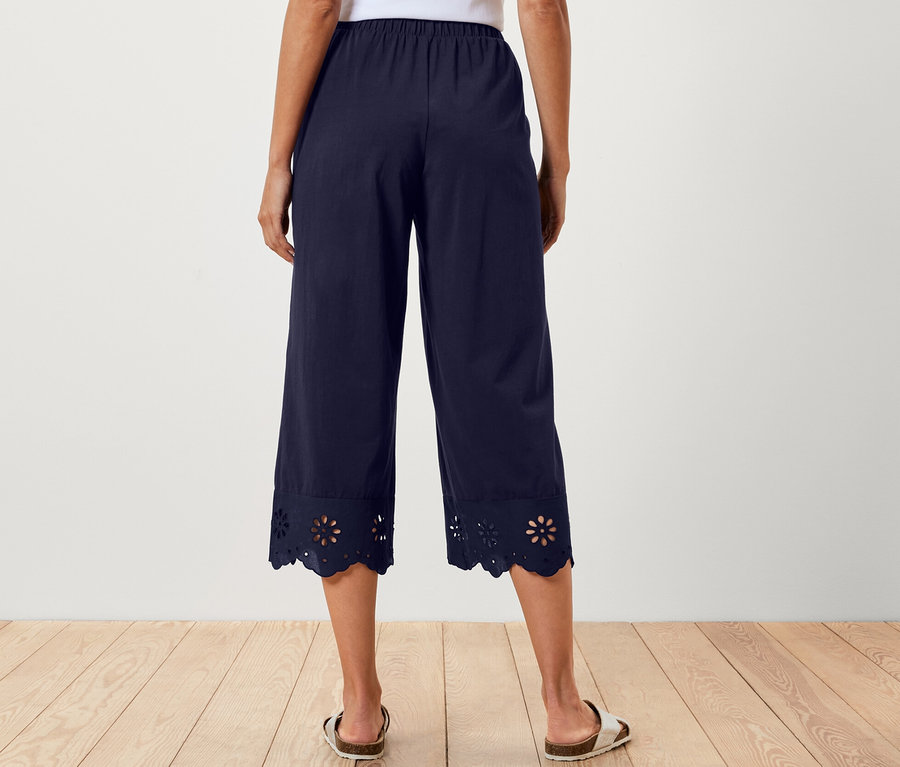 Femme de dos portant un haut blanc et un pantalon large bleu marine avec broderie à l'ourlet.