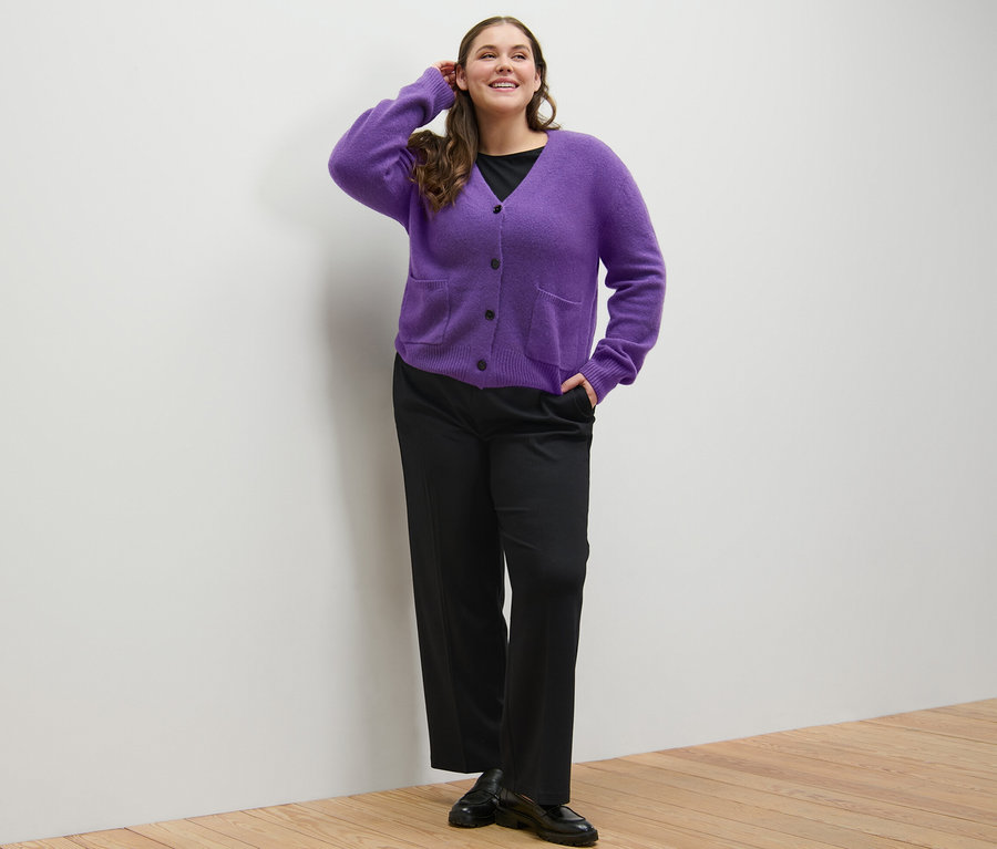 Femme posant en t-shirt manches 3/4 noir, pantalon en jersey confortable et jaquette en maille violette avec de la laine.