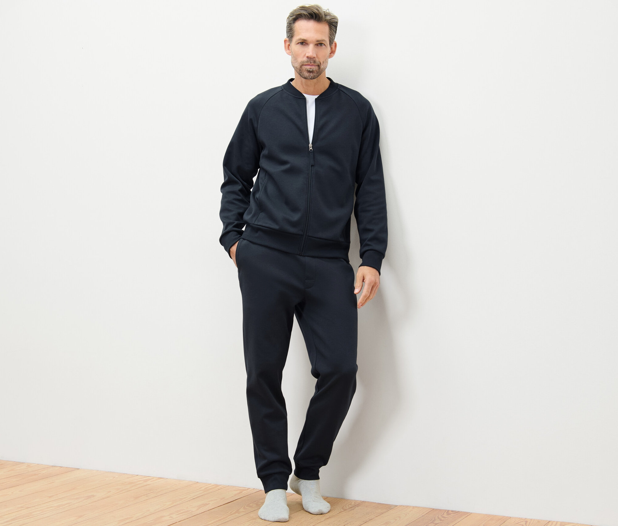 Un homme pose sur un plancher en bois en survêtement d’intérieur bleu marine.