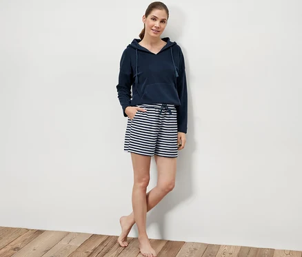 Une femme pose sur un plancher en bois en short éponge et sweat à capuche.