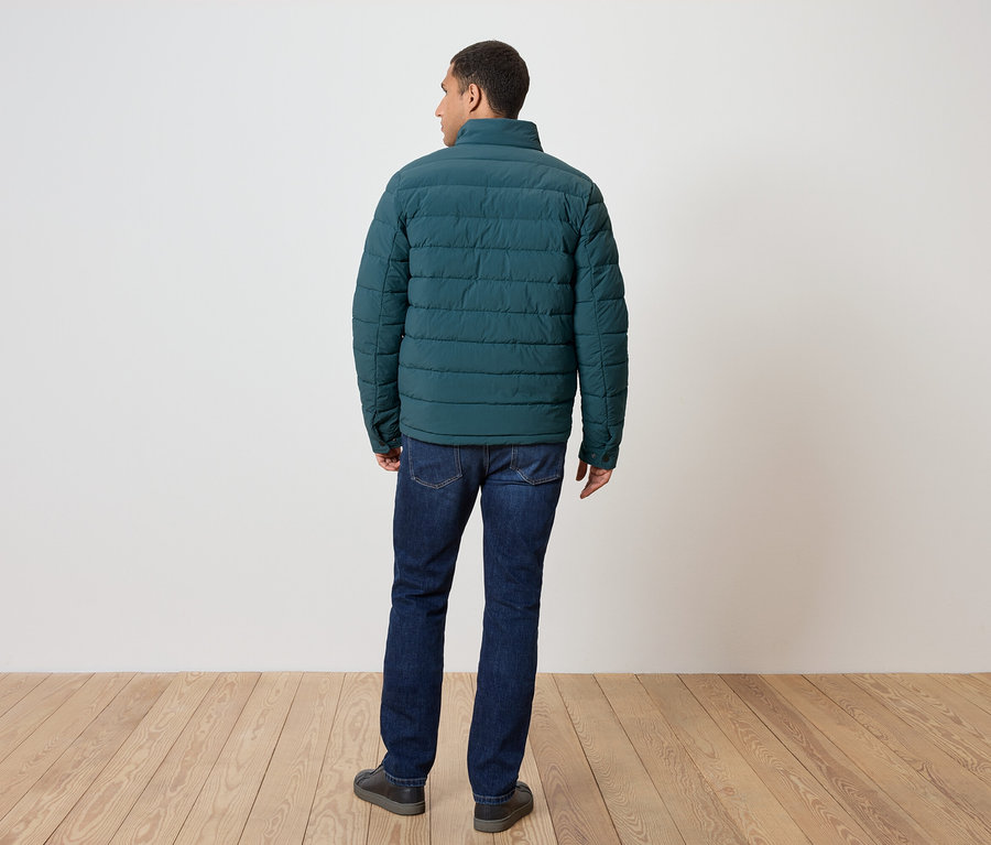 Un homme vu de dos porte une doudoune verte, un jean et des chaussures.