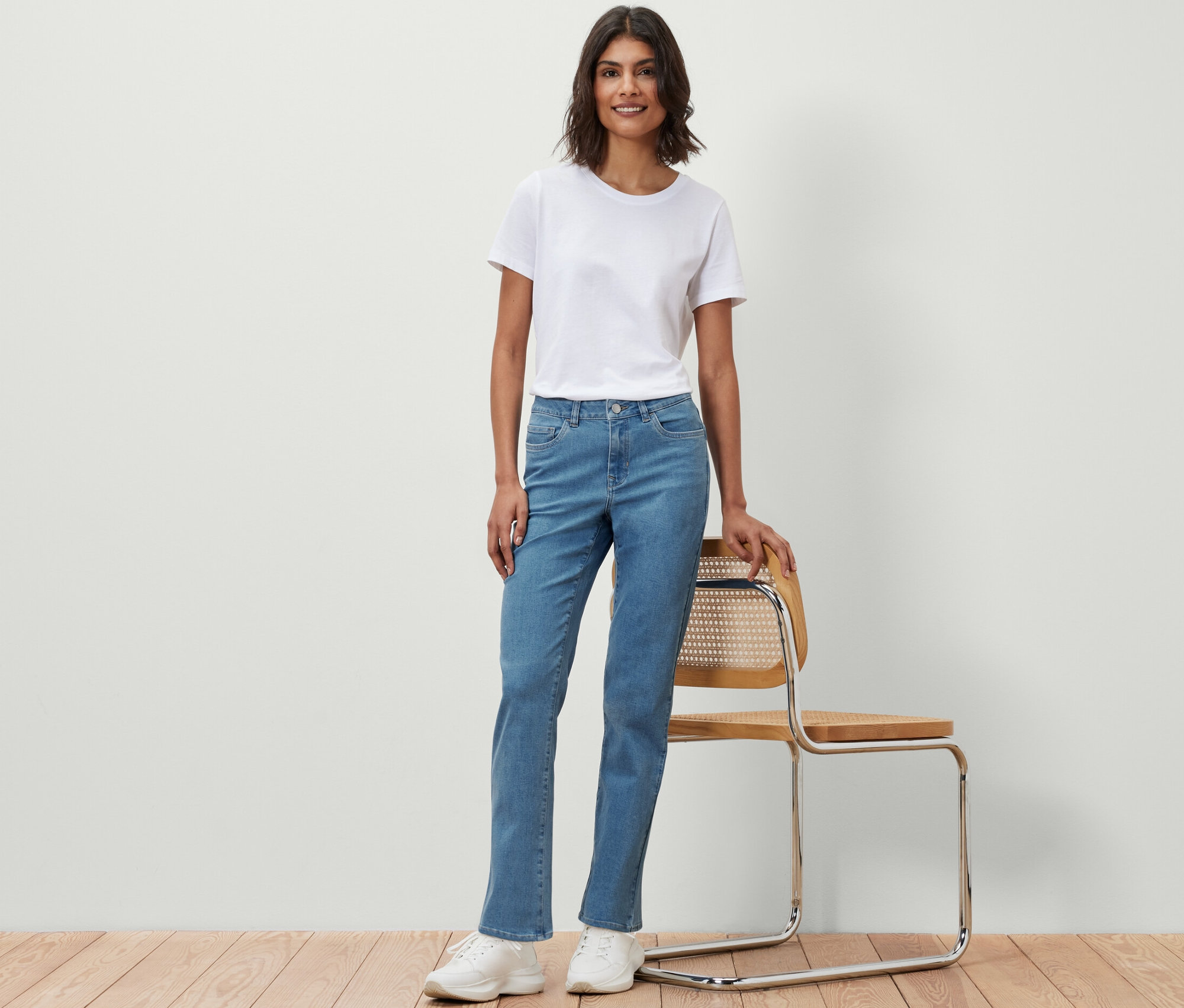 Une femme portant un t-shirt blanc et un jean droit - Coupe « Kira » se tient à côté d'une chaise.