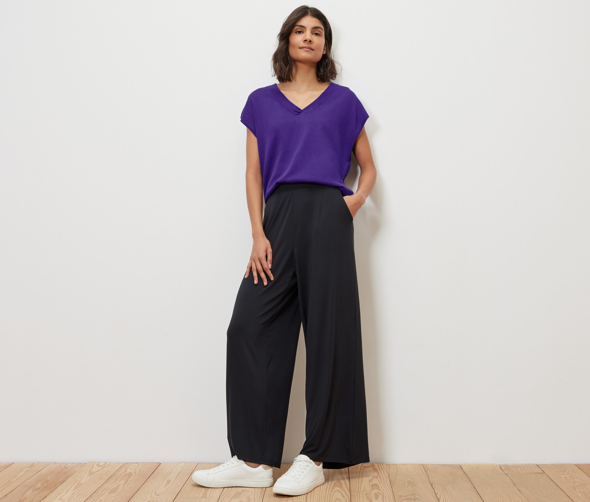 Femme posant en pull violet en maille fine à manches courtes et pantalon noir.