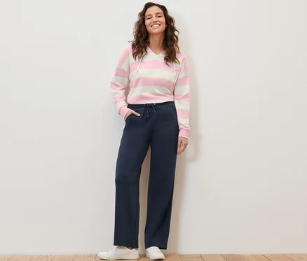 Une femme se tient debout et pose en pantalon de jogging bleu foncé et un sweat à capuche rayé.