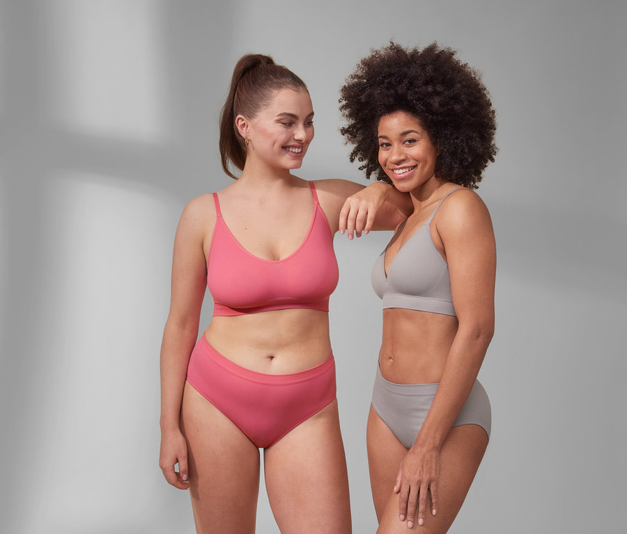 Deux femmes posent côte à côte. L'une porte un soutien-gorge à coques Seamless et une culotte Seamless rose vif. L'autre porte une brassière Seamless et une culotte Seamless grise.