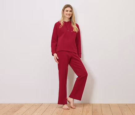Une femme pose en survêtement rouge composé d'un sweat à capuche et d'un pantalon de survêtement.