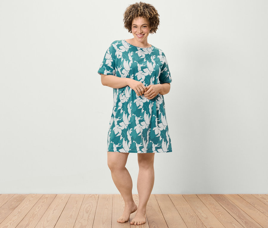Une femme debout porte une chemise de nuit à manches courtes avec un motif floral.