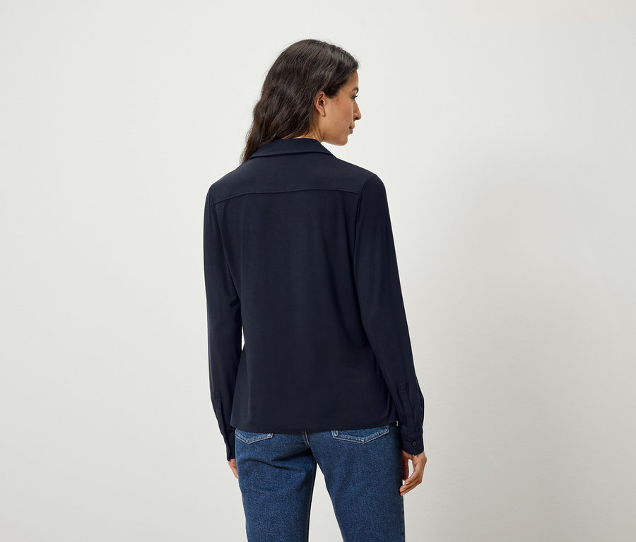 Vue arrière d'une femme aux cheveux foncés portant une chemise bleue et un jean.