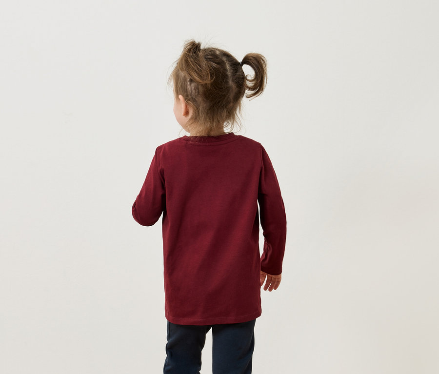 Vue de dos d'une petite fille avec des couettes portant un t-shirt à manches longues bordeaux et un pantalon bleu marine.
